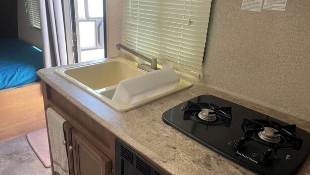 A compact kitchenette with a sink, stove, and window blinds. - Cozy Vegas Bunkhouse RV (Las Vegas)