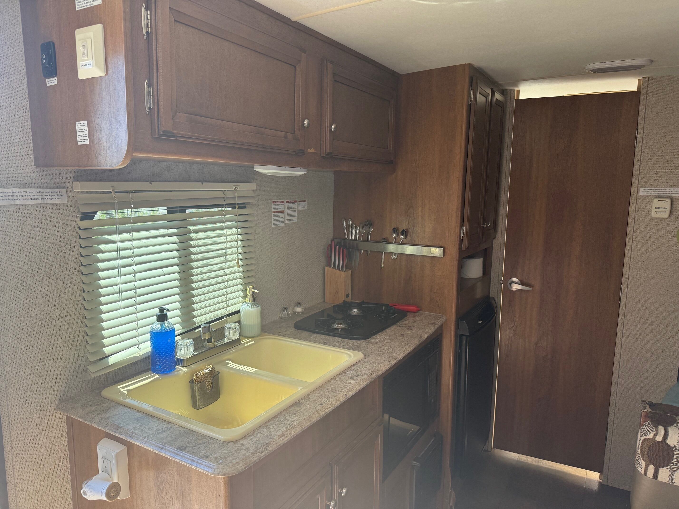 Une cuisine compacte pour camping-car, équipée d’un évier, d’une cuisinière et d’armoires en bois.