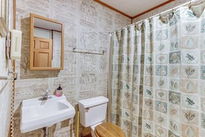 A bathroom with a wooden toilet, a white sink, and a shower curtain with a leaf pattern. - Creekside Family Home in Cleveland: Stay & Play! (Cleveland)