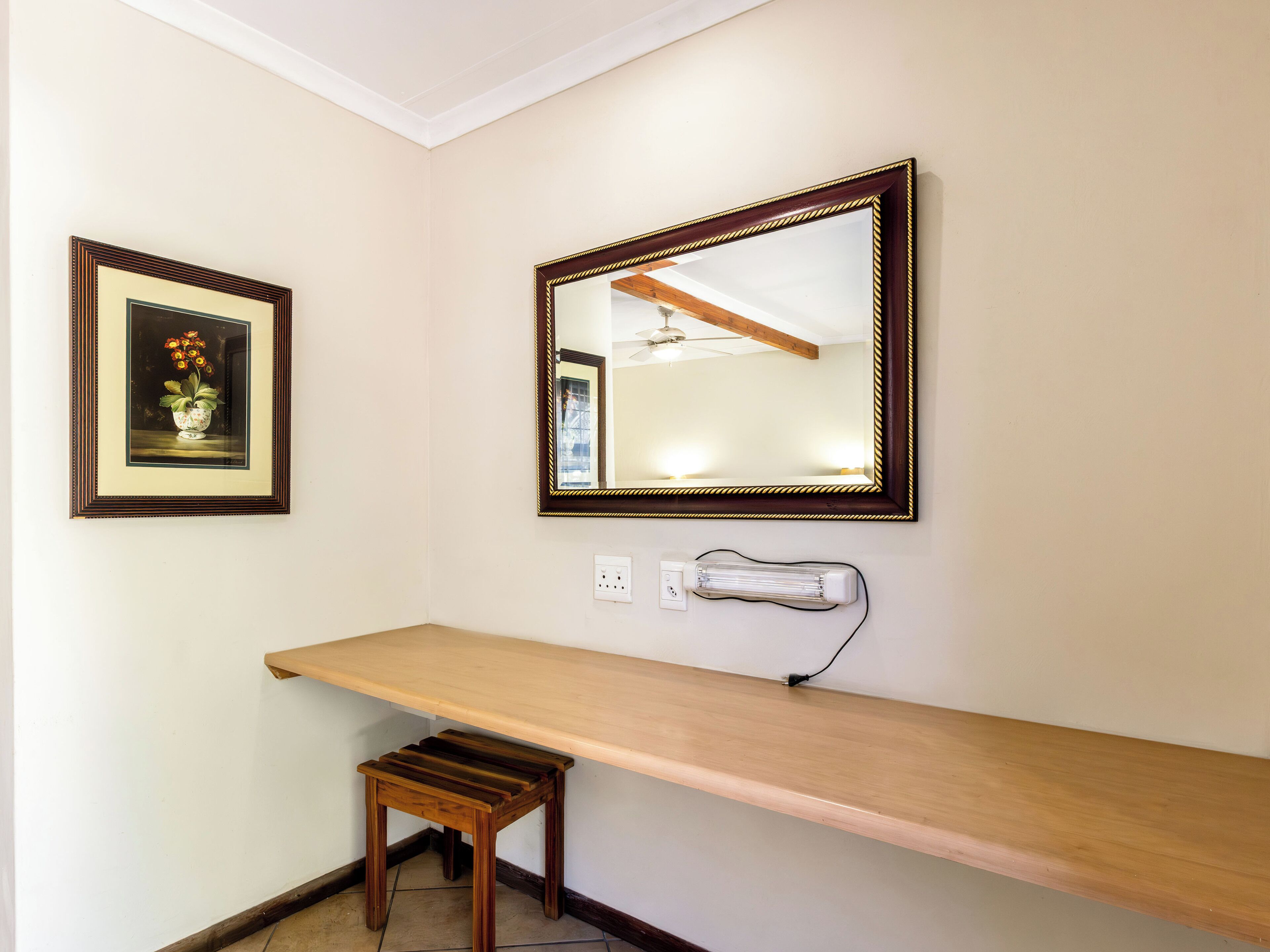Un coin de pièce avec un banc en bois, un tableau encadré et un miroir au mur.
