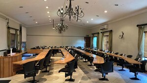 Ein Konferenzraum mit langem Tisch, Stühlen, einer Chandelüster und Fenstern mit Vorhängen.