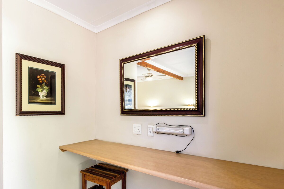 A corner of a room with a wooden bench, a framed picture, and a mirror on the wall.