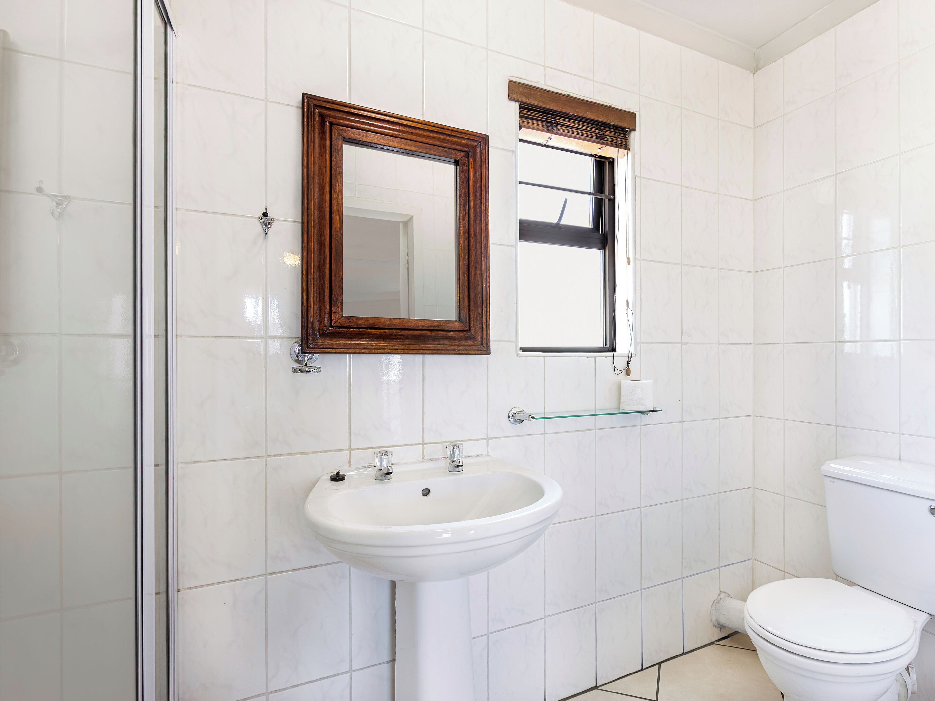 A bathroom with white tiles, a white sink, a toilet, and a mirror with a wooden frame.