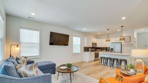 A modern living room with a sofa, armchair, and coffee table. A kitchen with white cabinets and a dining area with stools is visible in the background. - 2 Mi to UT: Modern Retreat w/ Covered Porch (Knoxville)