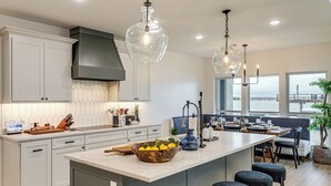 Une cuisine moderne dotée d’un grand îlot central, de luminaires suspendus et offrant une vue sur l’eau.