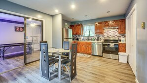 A modern kitchen with wooden cabinets, stainless steel appliances, and a glass dining table. - Poconos Family Home w/ Game Room + Community Perks (East Stroudsburg)
