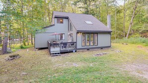 A two-story cabin with a deck and a chimney, surrounded by trees. - Poconos Family Home w/ Game Room + Community Perks (East Stroudsburg)