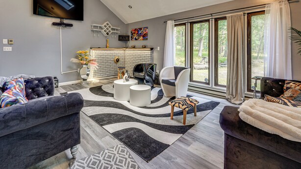A modern living room with a fireplace, comfortable seating, and large windows. - Poconos Family Home w/ Game Room + Community Perks (East Stroudsburg)