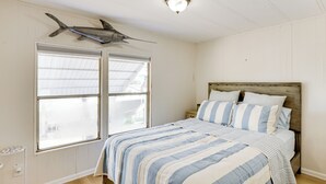 A bedroom with a bed, striped bedding, a wooden headboard, and a mounted shark on the wall. - Fish & Boat On-Site! Waterfront Florida Keys Home (Marathon)