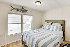 Un dormitorio con cama, ropa de cama a rayas, cabecera de madera y un tiburón colgado en la pared.