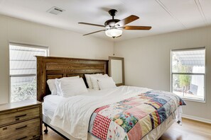 Ein Schlafzimmer mit einem hölzernen Kopfende, einer gesteppten Bettdecke, einem Deckenventilator und zwei Fenstern.