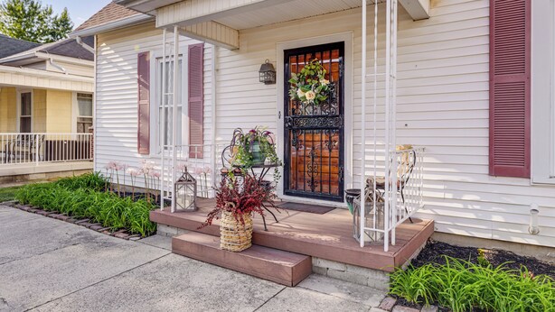 A house with a porch, a front door with a black metal gate, and a small garden area with plants. - Walkable Group Getaway w/ Bikes in West Liberty! (West Liberty)