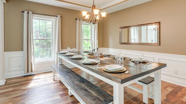 Comedor con una larga mesa dispuesta para seis personas, un candelabro y ventanas amplias con cortinas.