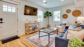 Un salon bien éclairé, doté d’un téléviseur à écran plat, d’un ventilateur de plafond, d’une table basse, d’un canapé et d’une grande fenêtre équipée de stores.