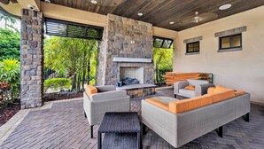 Un patio al aire libre con mobiliario de mimbre, una chimenea de piedra y vistas a la vegetación.