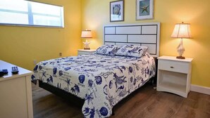 A bedroom with a bed, two bedside tables, a nightstand, a window with blinds, and two wall-mounted pictures. - Direct Ocean Complex! Diplomat 220-21 (Cocoa Beach)