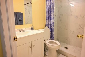 A bathroom with a white toilet, a sink with a mirror above it, and a shower area with a marble wall.