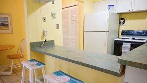 A kitchen with a refrigerator, stove, and a small bar stool with a beach-themed design. - Direct Ocean Complex! Diplomat 220-21 (Cocoa Beach)