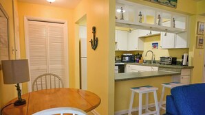 A compact kitchen with white cabinets, a dining table with chairs, and a blue sofa. - Direct Ocean Complex! Diplomat 220-21 (Cocoa Beach)