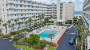 A multi-story hotel with a swimming pool, palm trees, and a view of the ocean.