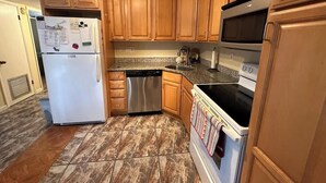 A kitchen with wooden cabinets, a stainless steel refrigerator, a dishwasher, a stove, and a microwave.