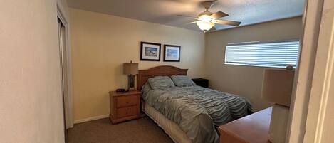 A bedroom with a bed, nightstands, a ceiling fan, a window with blinds, and a door.