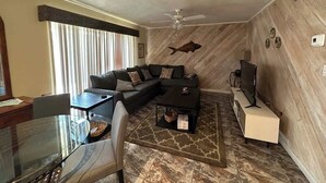 A living room with a sectional sofa, a glass coffee table, a television, and a patterned rug.
