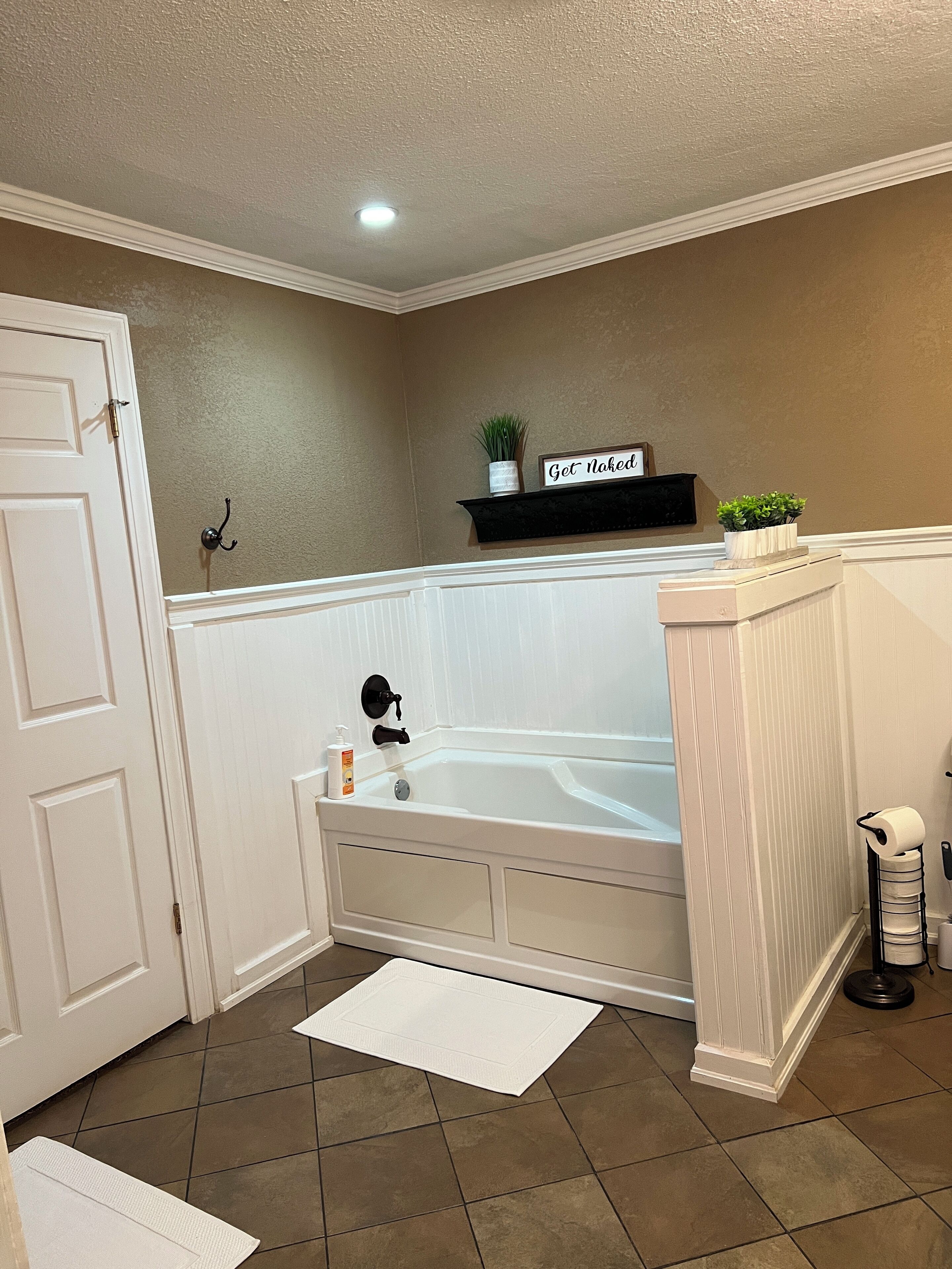 A bathroom with a bathtub, a towel rack, a shelf with plants, and a door.