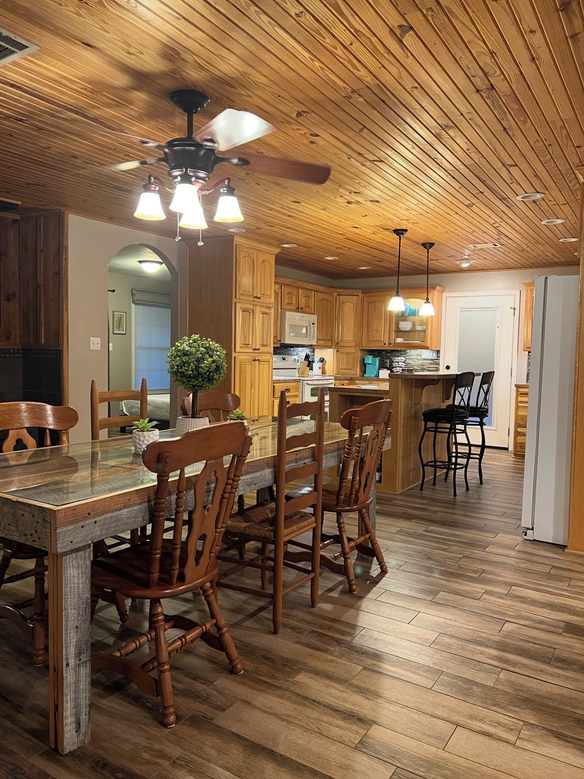 A wooden-paneled kitchen with a dining area, featuring a ceiling fan, pendant lights, and wooden flooring.