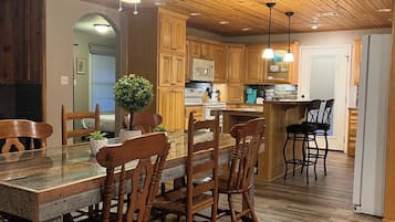 A wooden-paneled kitchen with a dining area, featuring a ceiling fan, pendant lights, and wooden flooring.
