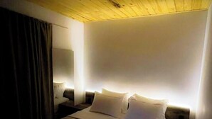 Une chambre d’hôtel avec un plafond en bois, un grand lit avec du linge de lit blanc, deux tables de chevet et une petite table de nuit avec une lampe.