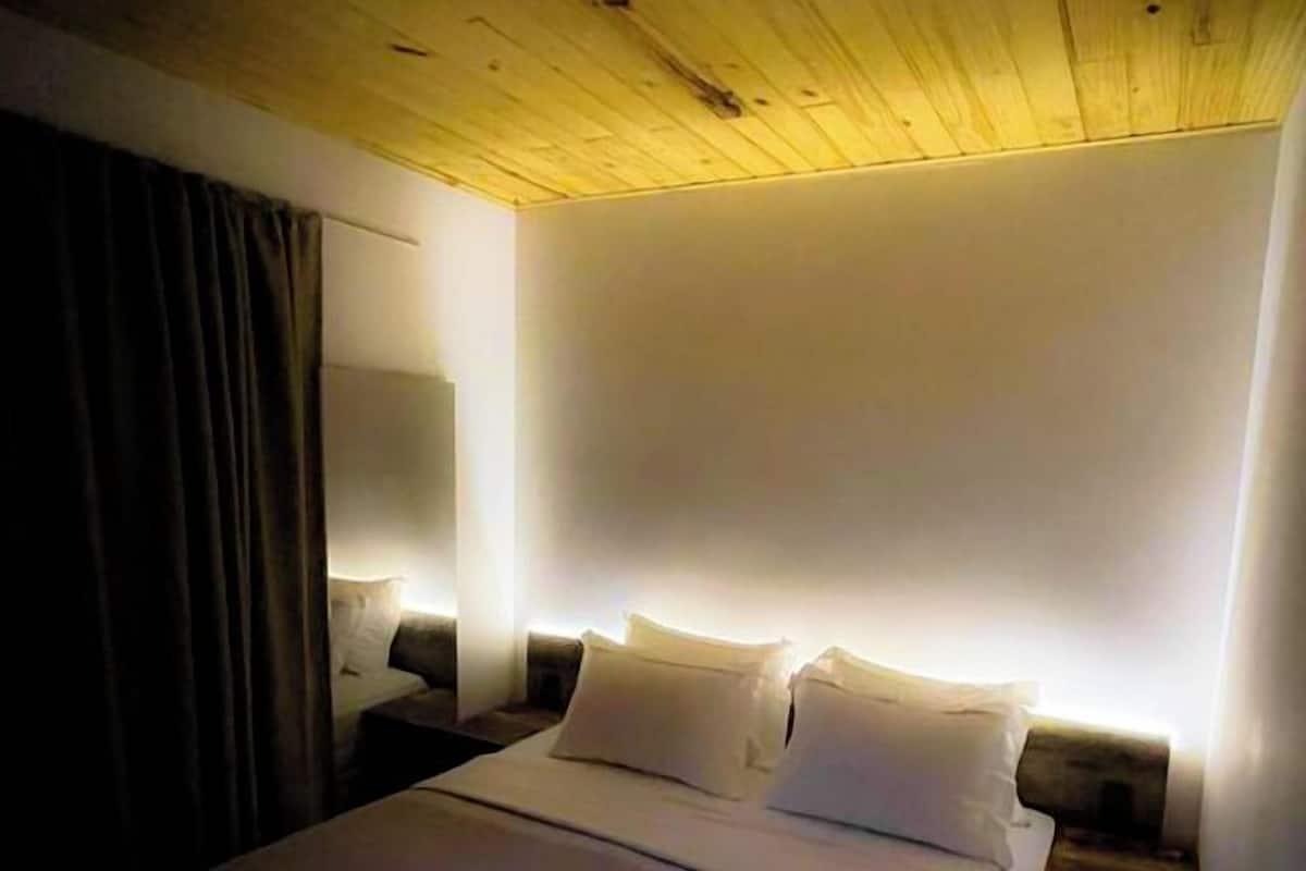 A hotel room with a wooden ceiling, a large bed with white linens, two bedside tables, and a nightstand with a lamp.