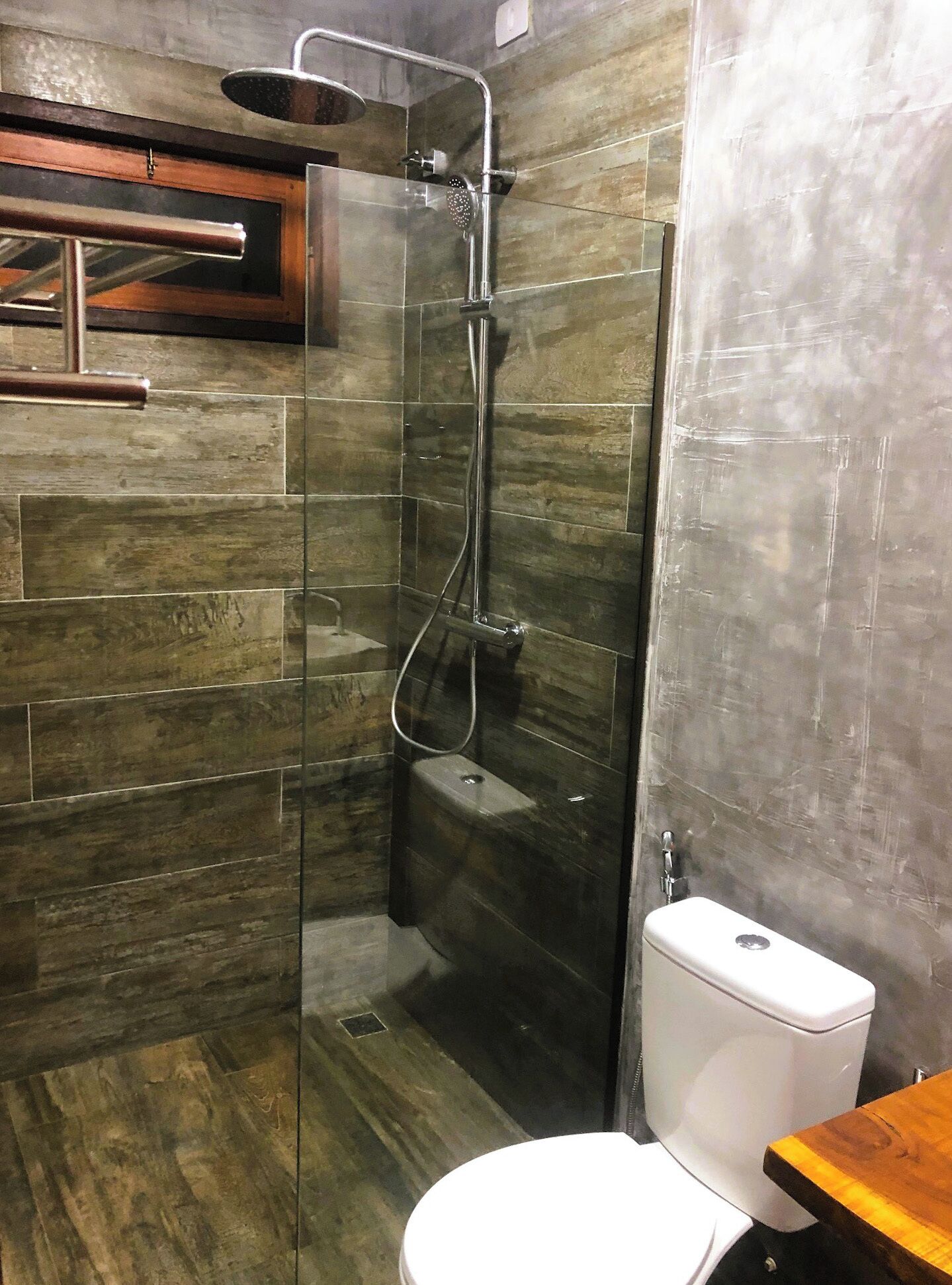 A modern bathroom with a glass-enclosed shower, a wooden vanity, and a white toilet.