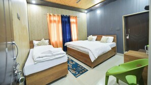 Une chambre d’hôtel avec deux lits en bois, un ventilateur de plafond et une chaise verte.
