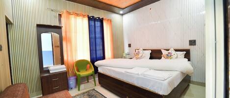 A bedroom with a large bed, a wooden ceiling fan, a green chair, and a small desk with a mirror.