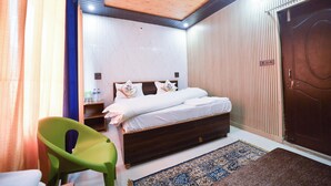 Une chambre avec un ventilateur de plafond en bois, un lit avec une literie blanche, une chaise verte et un tapis à motifs.
