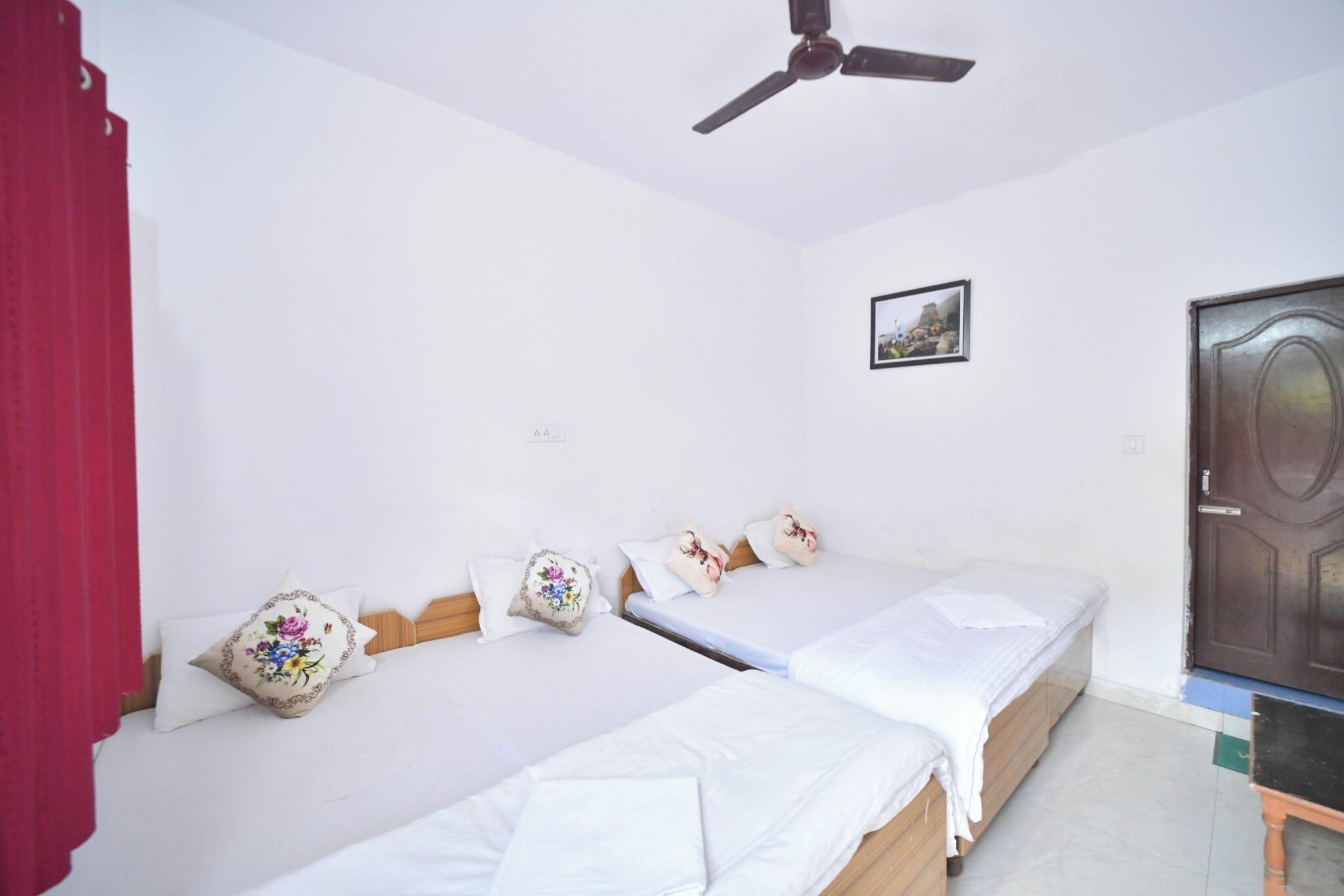 A hotel room with two single beds, a ceiling fan, a door, and a small framed picture on the wall.