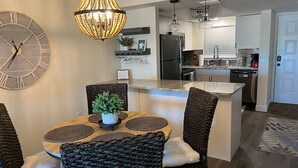 Una cocina moderna con una isla central, electrodomésticos integrados y un comedor con sillas de mimbre y una mesa redonda.