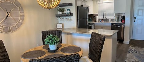 Una cocina moderna con una isla central, electrodomésticos integrados y un comedor con sillas de mimbre y una mesa redonda.