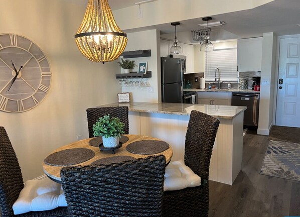 A modern kitchen with a central island, built-in appliances, and a dining area with wicker chairs and a round table.