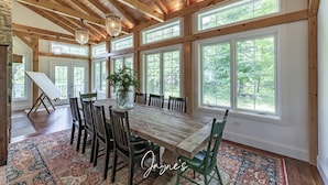 Un vaste espace dédié à la salle à manger, avec une grande table en bois, de nombreuses chaises et une vue sur l’extérieur grâce à de grandes fenêtres.