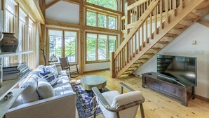 Un salon spacieux avec un escalier en bois, de grandes fenêtres, un canapé, une table basse et un téléviseur à écran plat.