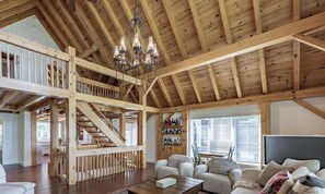 A spacious loft-style room with a wooden staircase, a chandelier, and a cozy seating area with a fireplace.