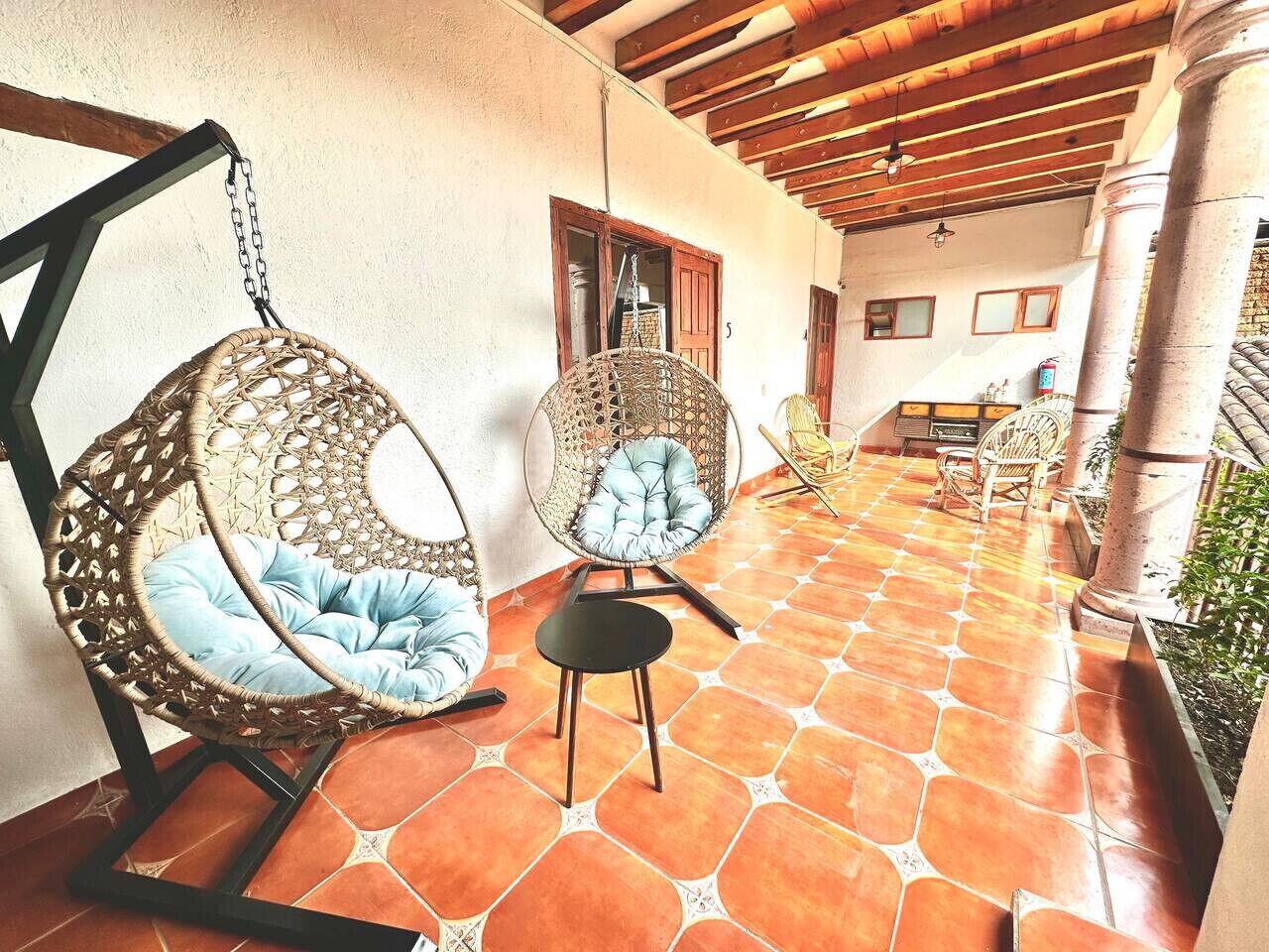 A covered outdoor area with wicker chairs and a small table, a tiled floor, and a wooden ceiling structure.