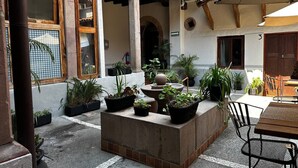 Ein Innenhof mit Holztisch und -stühlen, umgeben von Kübelpflanzen und einer Steinfontäne.