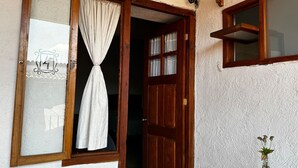 A wooden door with a white curtain, a window with a decorative frame, and a small table with a green vase.