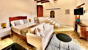 A bedroom with a large bed, a sofa, a TV, and a staircase leading to an upper level.