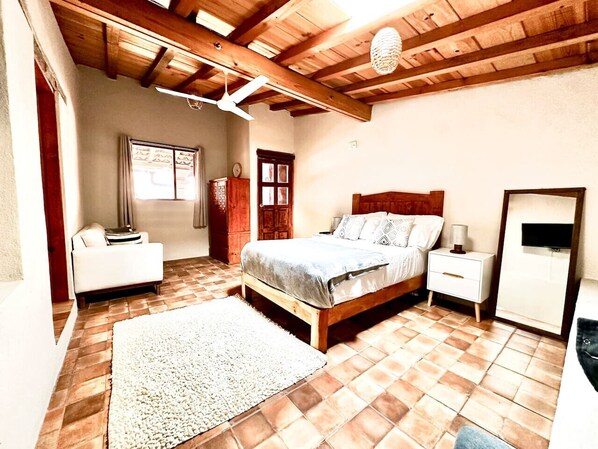 A bedroom with a wooden bed, a nightstand, a white dresser, a window, and a door.