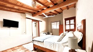 Ein Schlafzimmer mit Holzboden, einem Bett mit weißer Bettwäsche, einer Nachttischlampe und einem an der Wand befestigten Flachbildfernseher.
