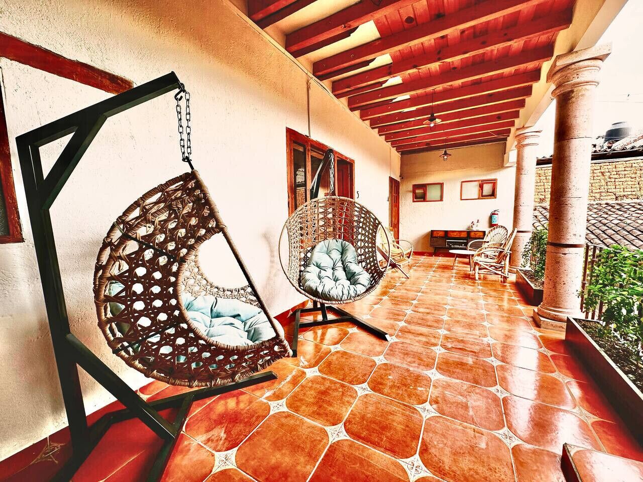Un patio techado con dos sillas colgantes de mimbre, piso de baldosas y pared de ladrillo.